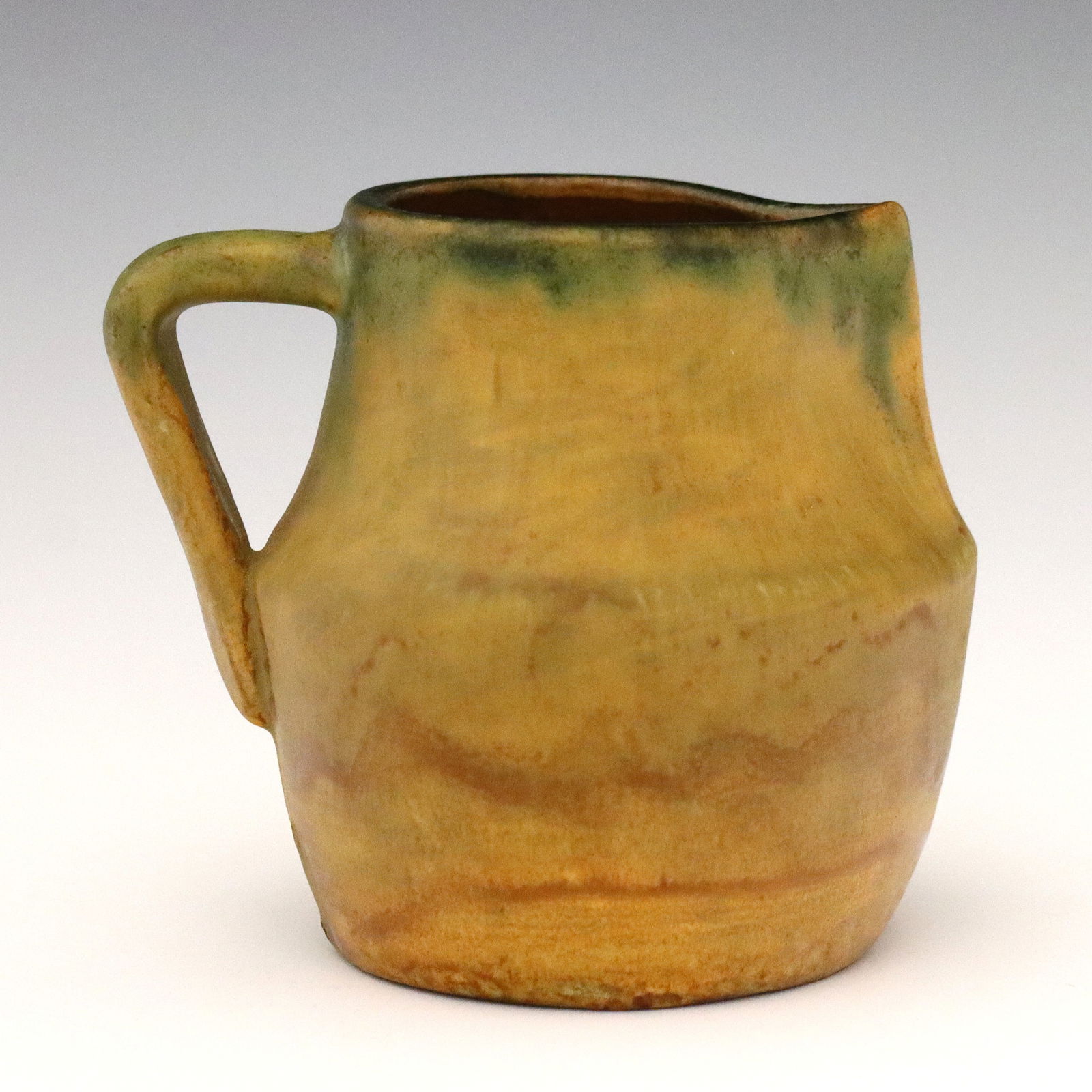 Early Pewabic Pottery Creamer: An early 20th century Pewabic Pottery creamer, c. 1905. Bulbous form with a strap handle and matte glaze in mottled shades of Brown and Green. Impressed Pewabic Maple Leaf mark used between 1903
