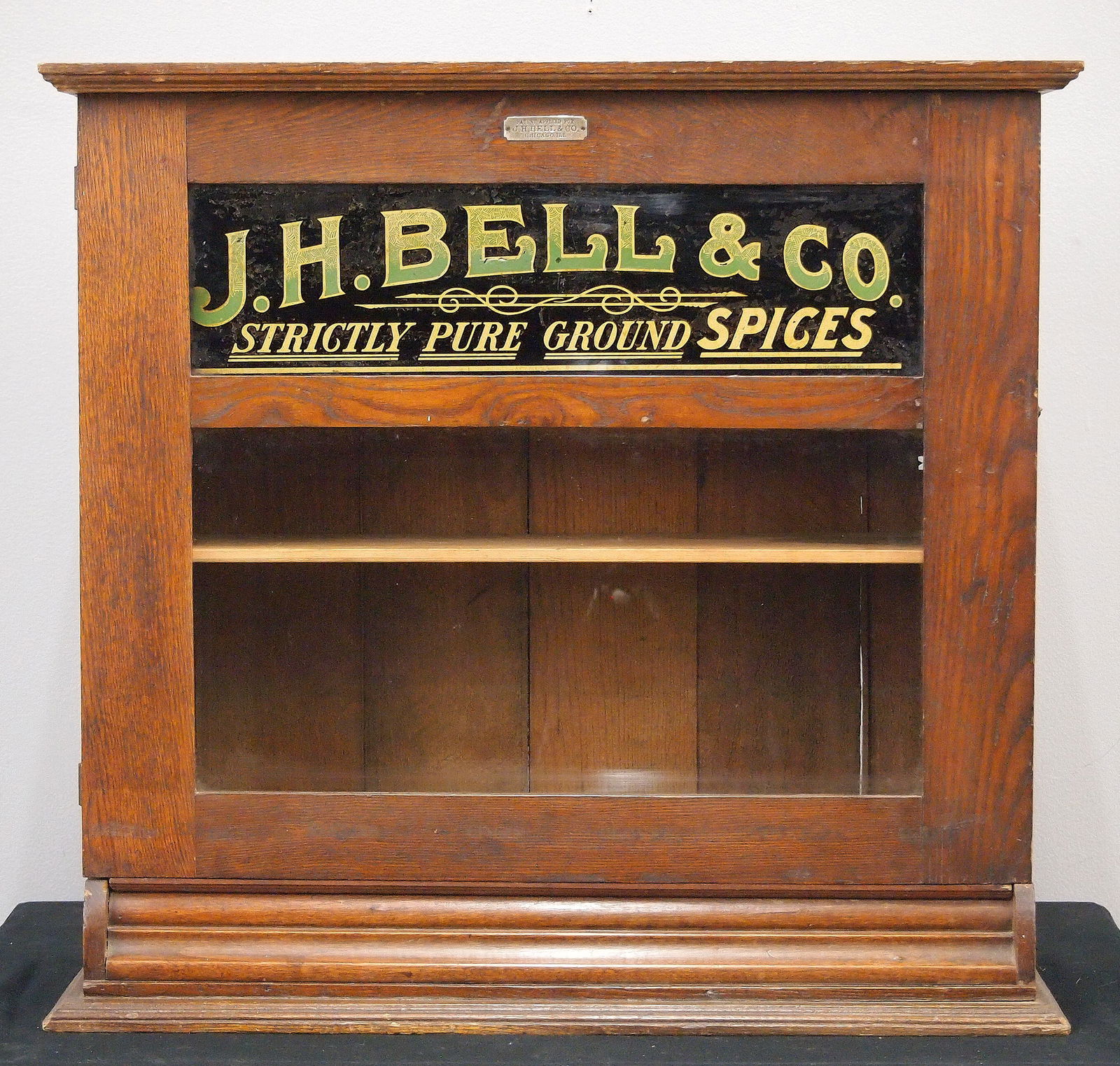 J. H. Bell Store Display case: A turn of the century J. H. Bell store display cabinet. Oak construction with hinged door and two-glass panels, the upper with reverse painted advertising "J. H. Bell & Co, Strictly Pure Ground