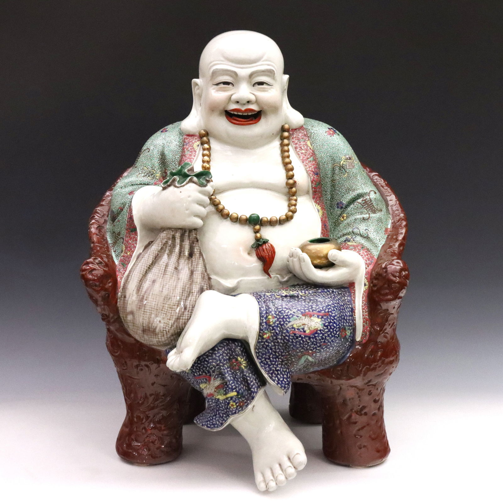 Chinese Porcelain Laughing Buddha: A large Chinese Famile Rose porcelain figure of a Laughing Buddha. Depicted seated in a "carved" armchair with scenic panels, holding a cloth sack representing his origin as the monk Budai in one