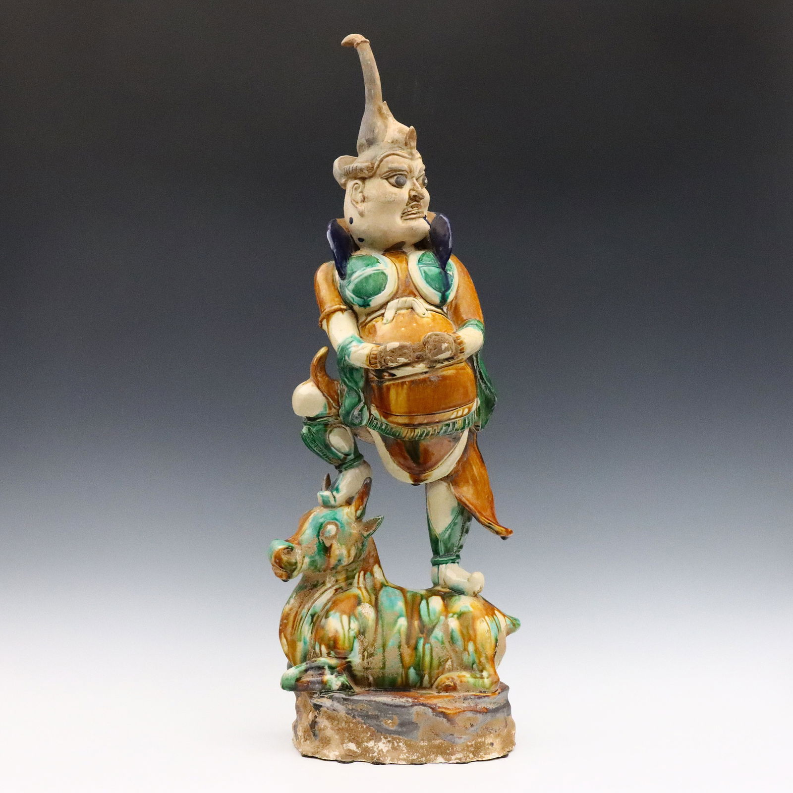 Chinese Terracotta Tomb Figure: A Chinese Tang style Terracotta tomb figure. Depicts a Buddhist Guardian standing on the back of a horse in Sancai glaze. Layer of clay applied over glaze crumbling, some craquelure. 28 3/4" high. EST