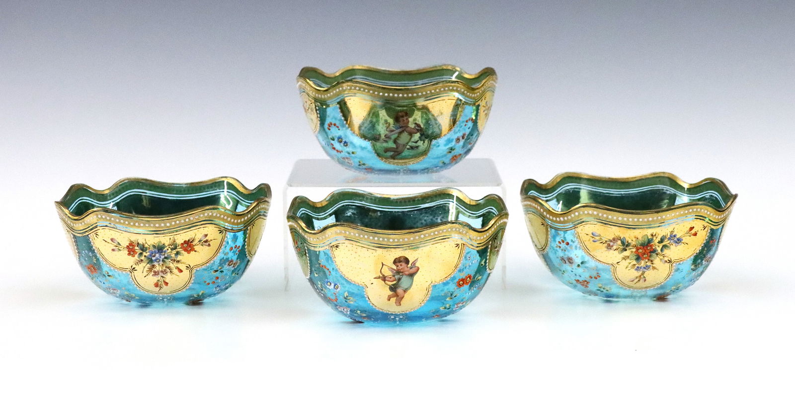 4 Bohemian Glass Finger Bowls: A set of four turn of the century Bohemian Art Glass finger bowls. Blue glass bowls with ruffled rim and enameled scenic panels of alternating Cherubs and florals with Gilded accents. Unmarked. 