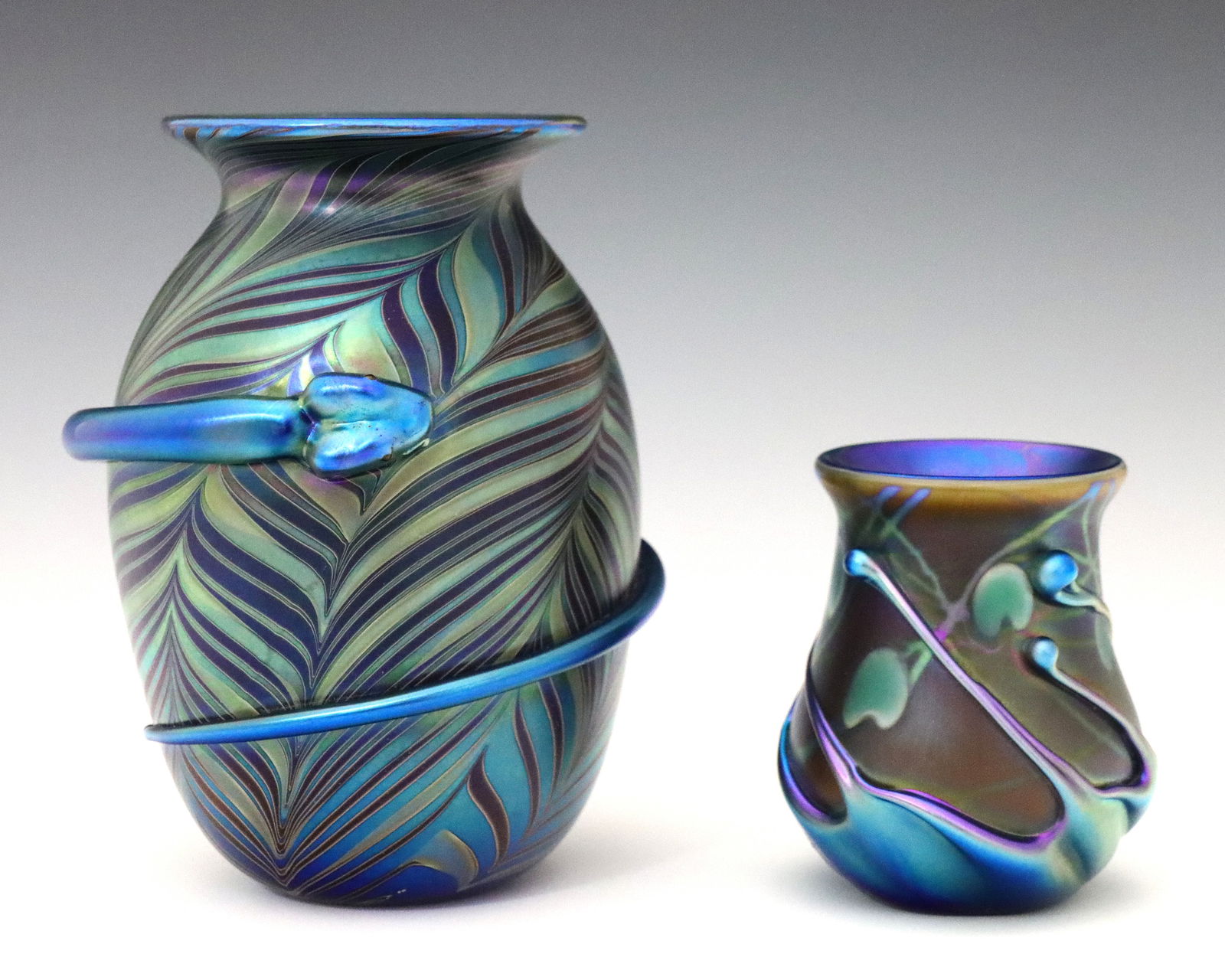 2 Pcs Lundberg Studios Glass: Two 1970's Lundberg Studios Art Glass vases. Blue glass bodies with Iridescent finish in shades of Purple and Green with applied decoration. Include a diminutive vase with Heart and Vine design, and a