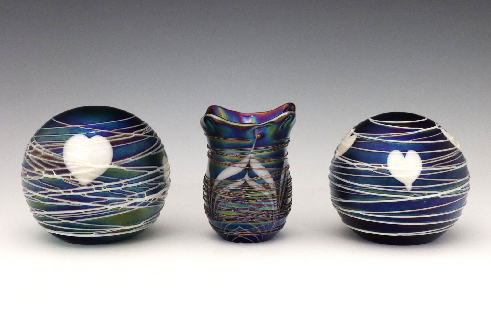 3 pcs Terry Crider Glass: Terry Crider, American, 20th/21st century. Three pieces of late 20th century Iridescent glass in shades of Blue, Green, and Purple with applied threading decoration. Includes two paperweights with Hea