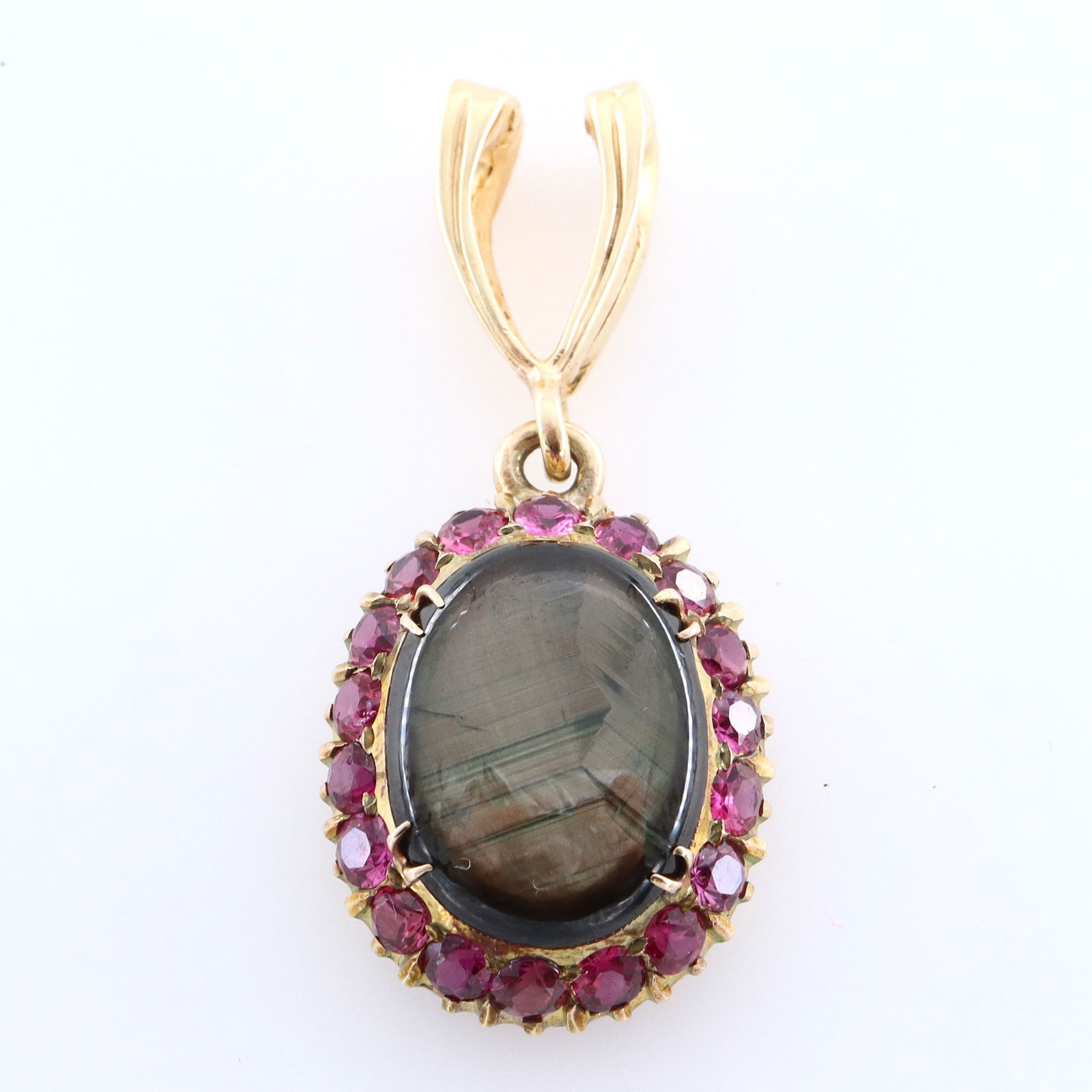 14k Gold, Black Star Sapphire & Ruby Pendant: A 14k Gold necklace pendant with Black Star Sapphire and Rubies. Features a 2.2 x 5.7 mm Black Star Sapphire cabochon surrounded by eighteen round cut prong set Rubies on a hinged, wishbone form hange
