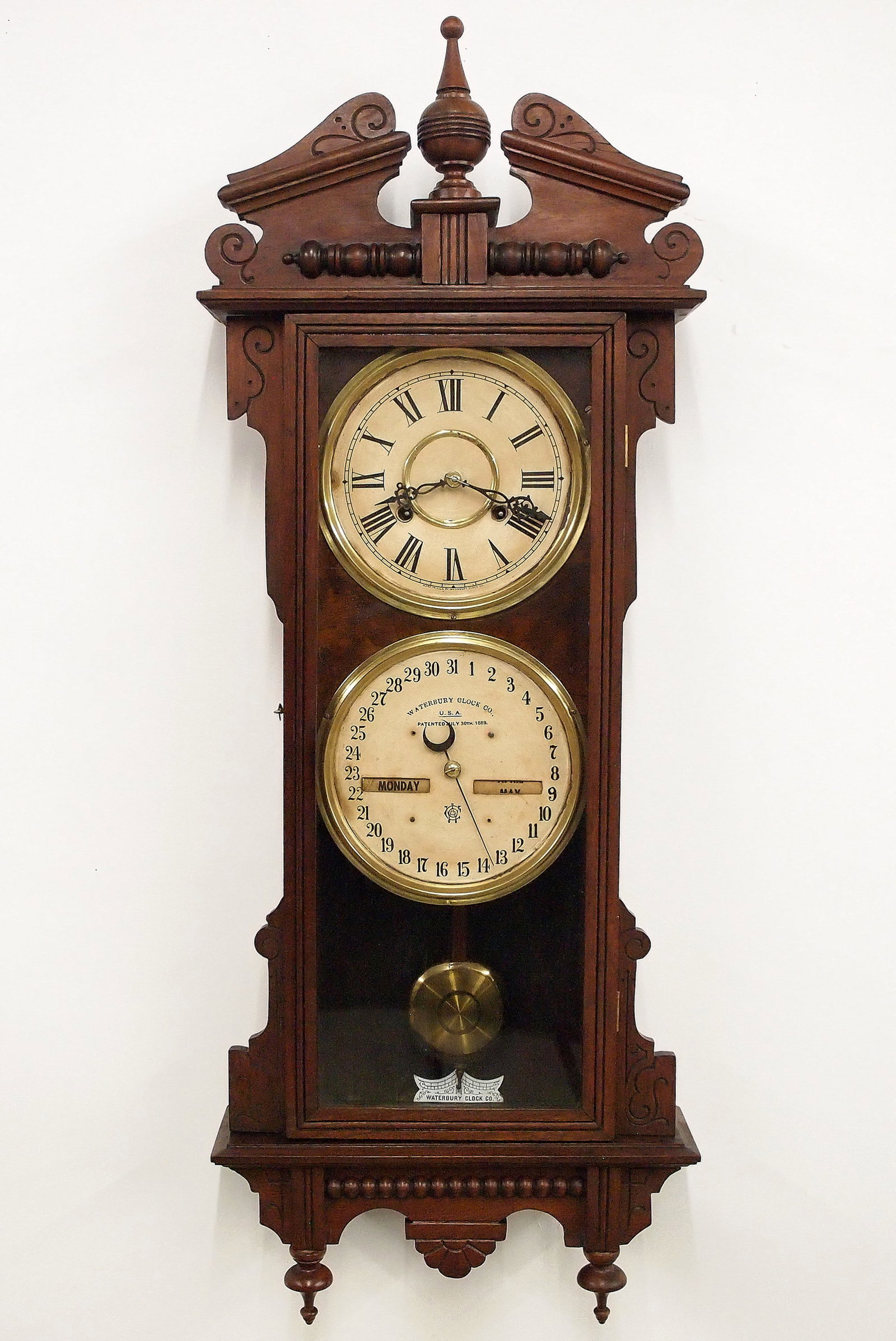Waterbury Model 33 Calendar Wall Clock: A late 19th century Waterbury Regulator No. 3 model wall clock. 8-day time and strike movement with lower calendar mechanism, papered metal dials with Roman/Arabic numerals. Walnut case with shaped
