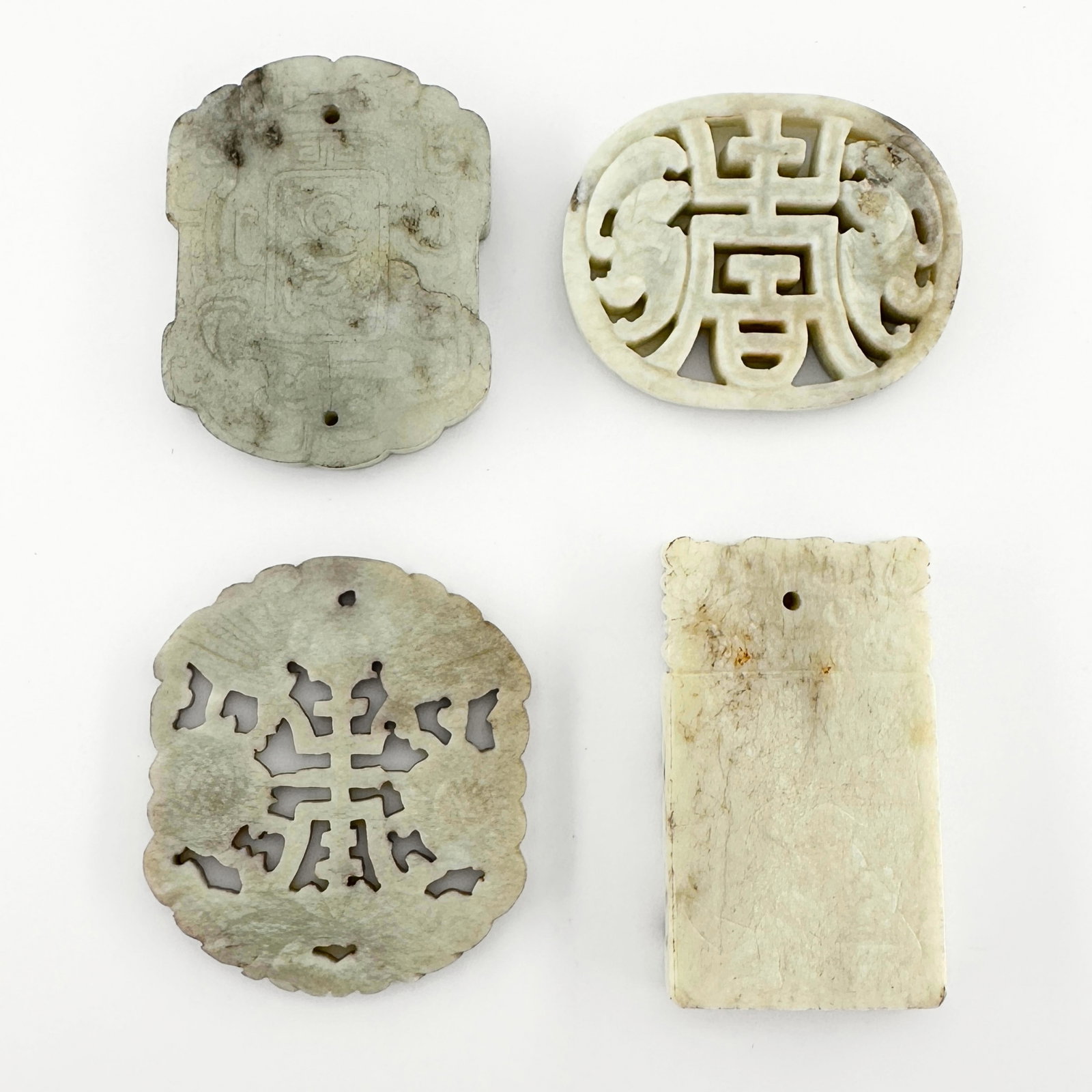 4 Chinese Carved Jade Pendants: Four Chinese carved Jade pendants. Reticulated and carved designs with auspicious characters and carved decoration depicting a dragon, bat, figural genre scene and florals. Surface wear, small inclusi