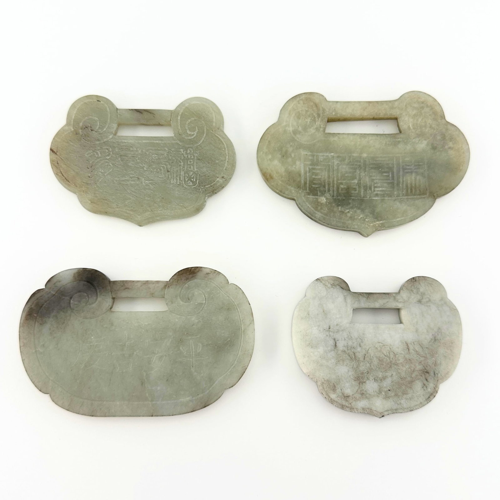 4 Chinese Carved Jade Pendants: Four Chinese carved Jade pendants. Carved designs with auspicious characters and relief carved decoration depicting peaches and flowering prunus. Some surface wear, inclusions and minor damage, areas 