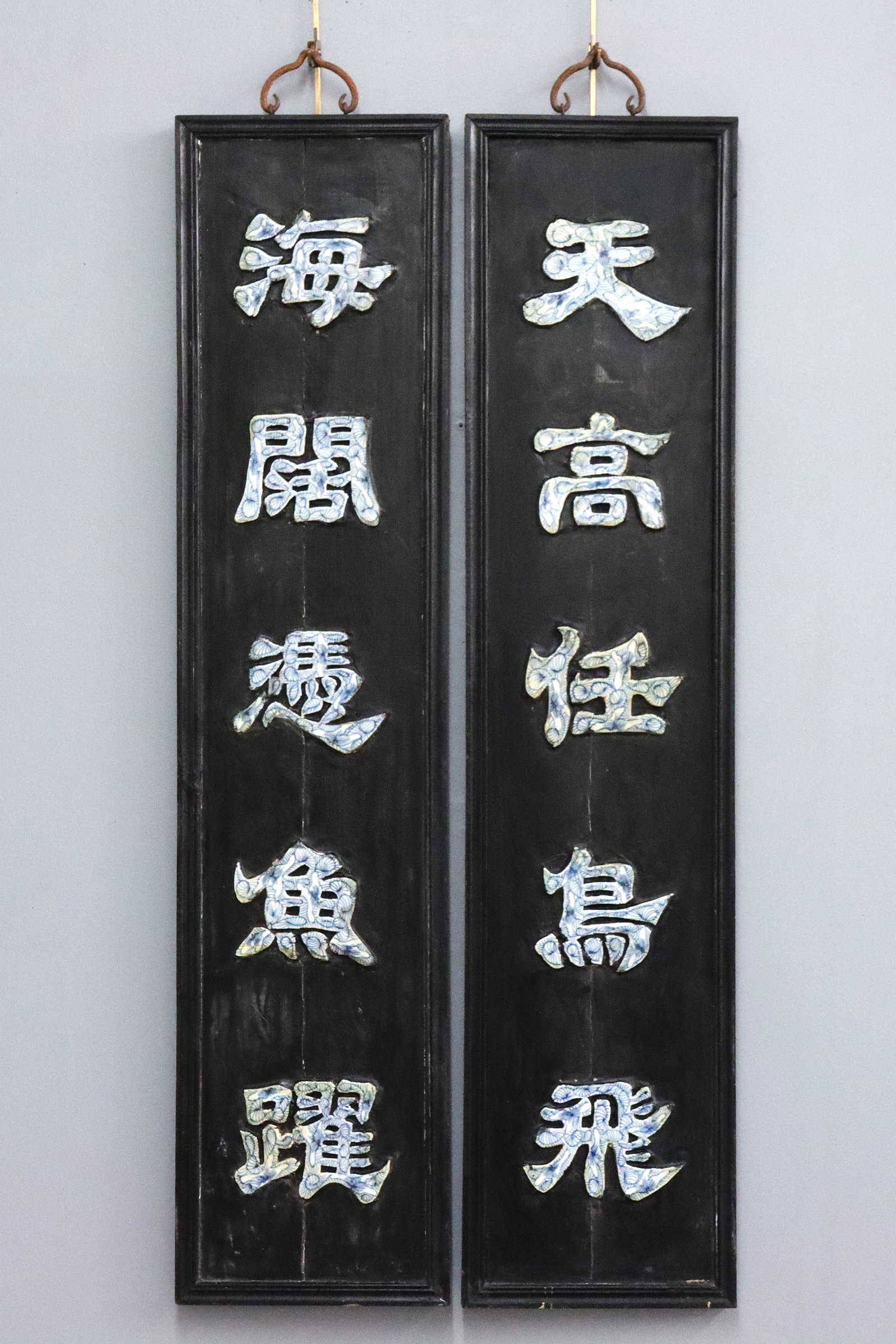 2 Chinese Hanging Panels: A pair of Chinese hanging panels. Molded hardwood frames featuring five inlaid Blue and White porcelain calligraphy plaques. Old Black painted finish with some wear, minor damage, both with shrinkage 
