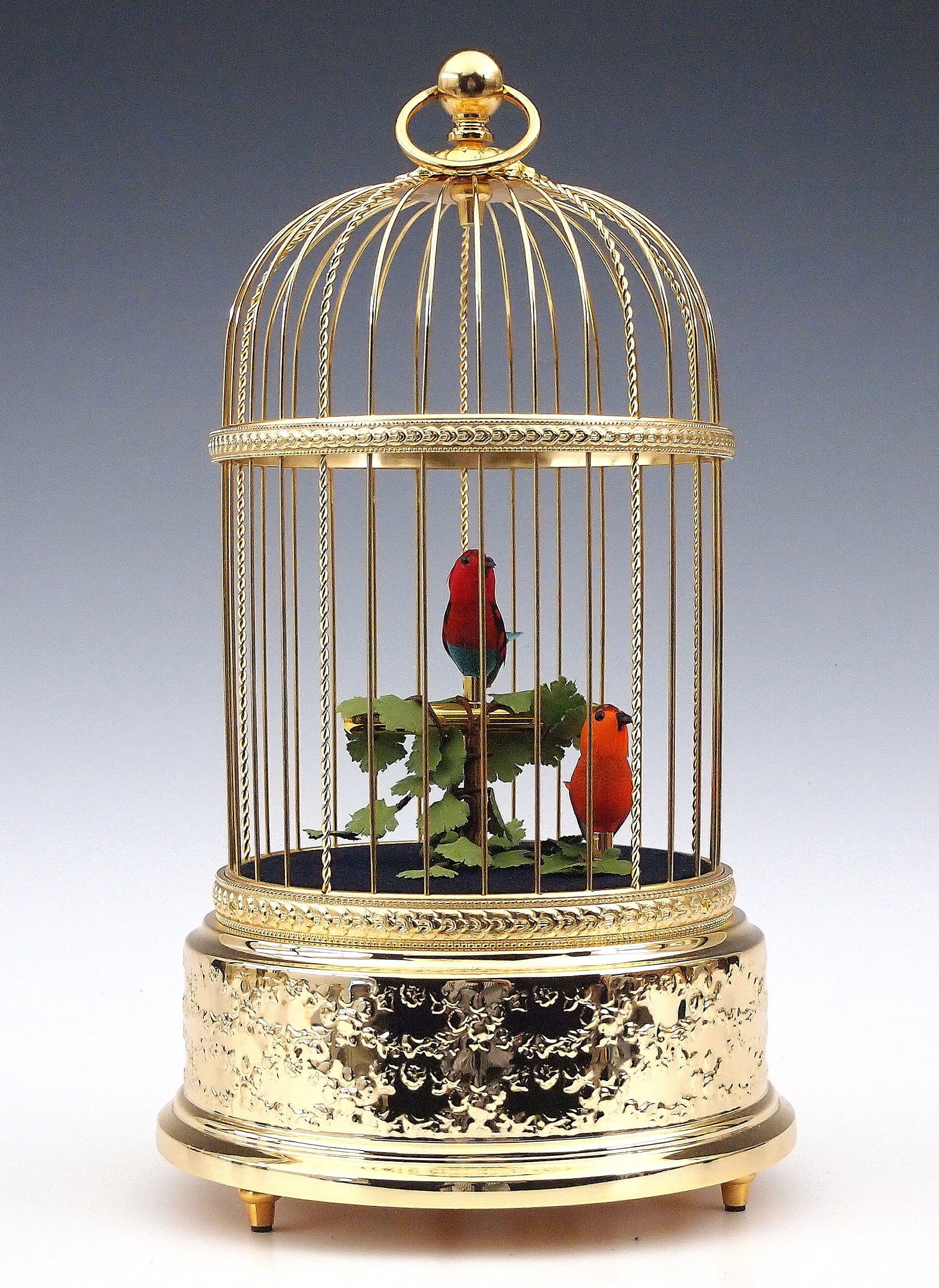 Reuge Singing Bird Automaton: A late 20th century Reuge Swiss Singing Bird Automaton. Wind-up singing birds with vibrant feathers within a Gilded metal cage. Stamped with maker's mark and "14994" at the underside. Winds and functi