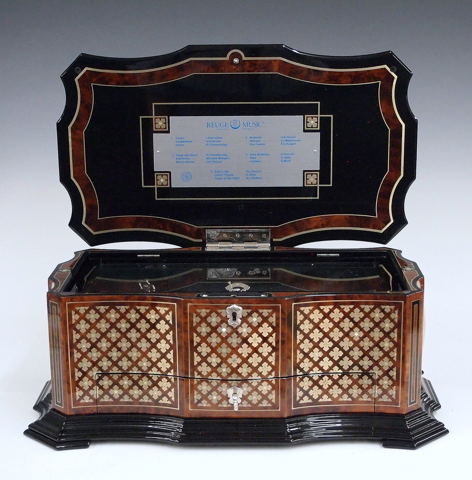 Reuge Swiss Music Box: A late 20th century Reuge Swiss Music Box. Burl Walnut construction with inlaid Mother of Pearl and lacquered decoration, features a hinged top and single drawer that opens to reveal four additional c