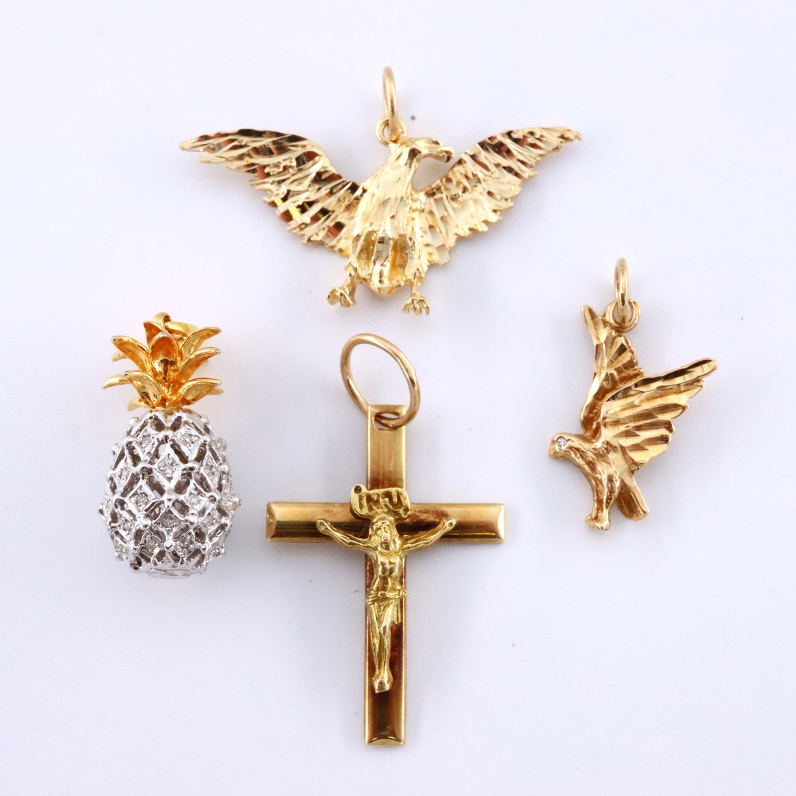 4 14k Gold Charms & Pendants: Four 14k Gold necklace charms and pendants. Includes a two-tone pineapple, two eagles, and a crucifix. Each marked or tested "14k". 12.8 grams total. Minor wear. Up to 1 1/2" high. ESTIMATE $1,000-1,5