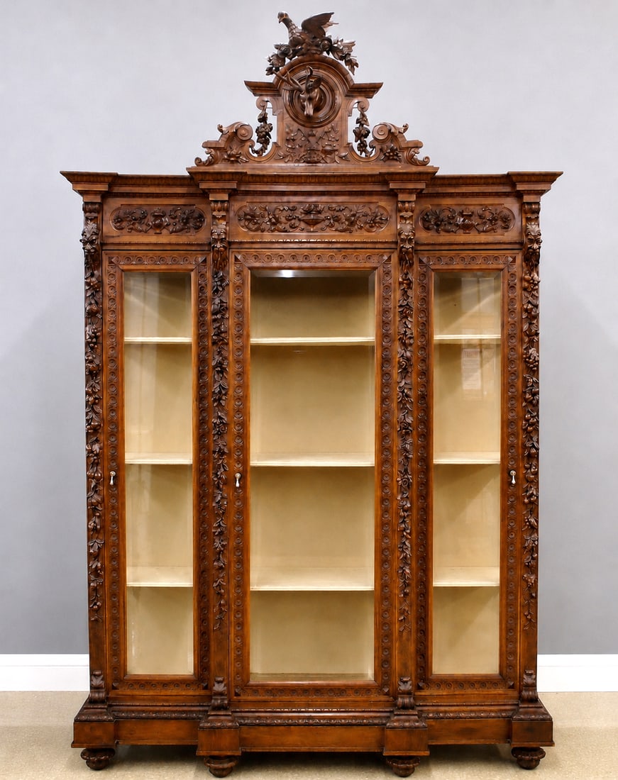 Victorian Walnut Library Case: A late 19th century Victorian Period breakfront library case. Walnut construction with extensive hand carved detail features a carved crown with songbird, Stag head and floral swags over a molded crow