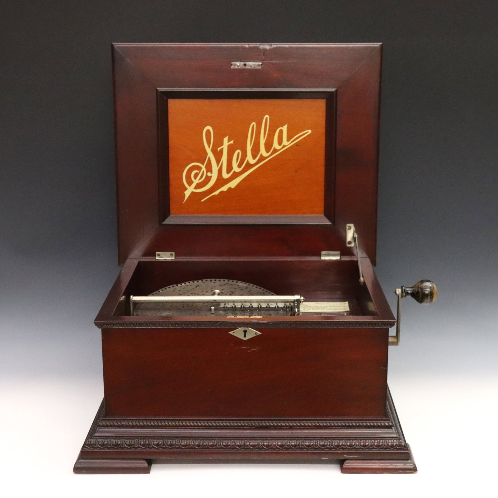 Stella Music Box: A turn of the century Stella music box. Swiss made disc player housed within a mahogany case with egg and dart, gadroon, and acanthus motifs overall complete with crank with knob handle; includes one 