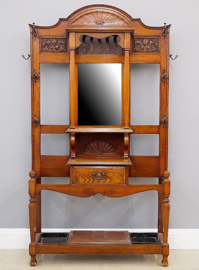 Oak Hall Tree: A turn of the century English hall tree. Oak construction features an arched crown with carved shell over a beveled glass mirror flanked by columns and carved foliate panels above a dovetailed glove d