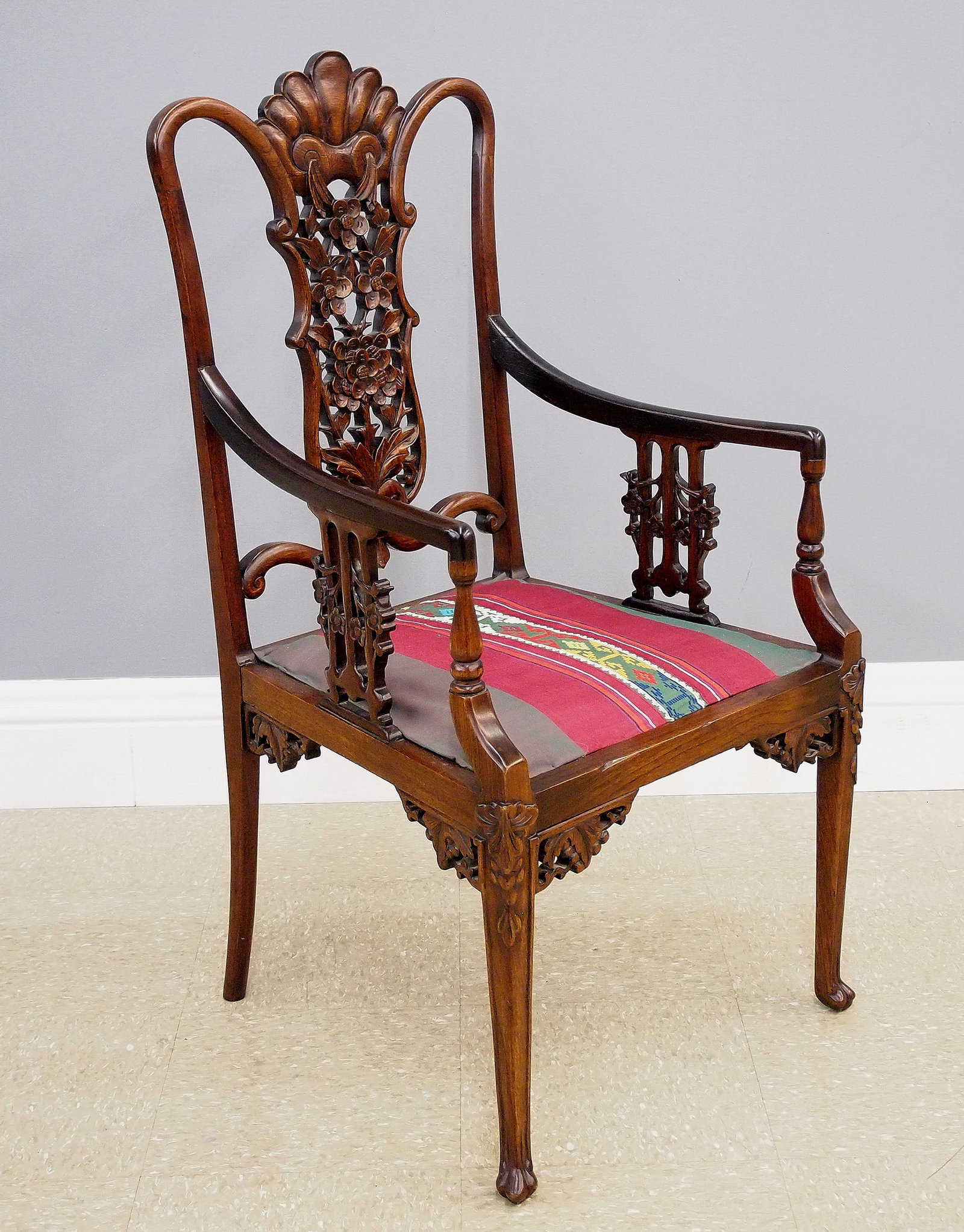 Chinese Armchair: A turn of the century Chinese armchair. Rosewood construction with carved detail features an open back with reticulated center splat, shaped arms with carved supports, upholstered seat and slender
