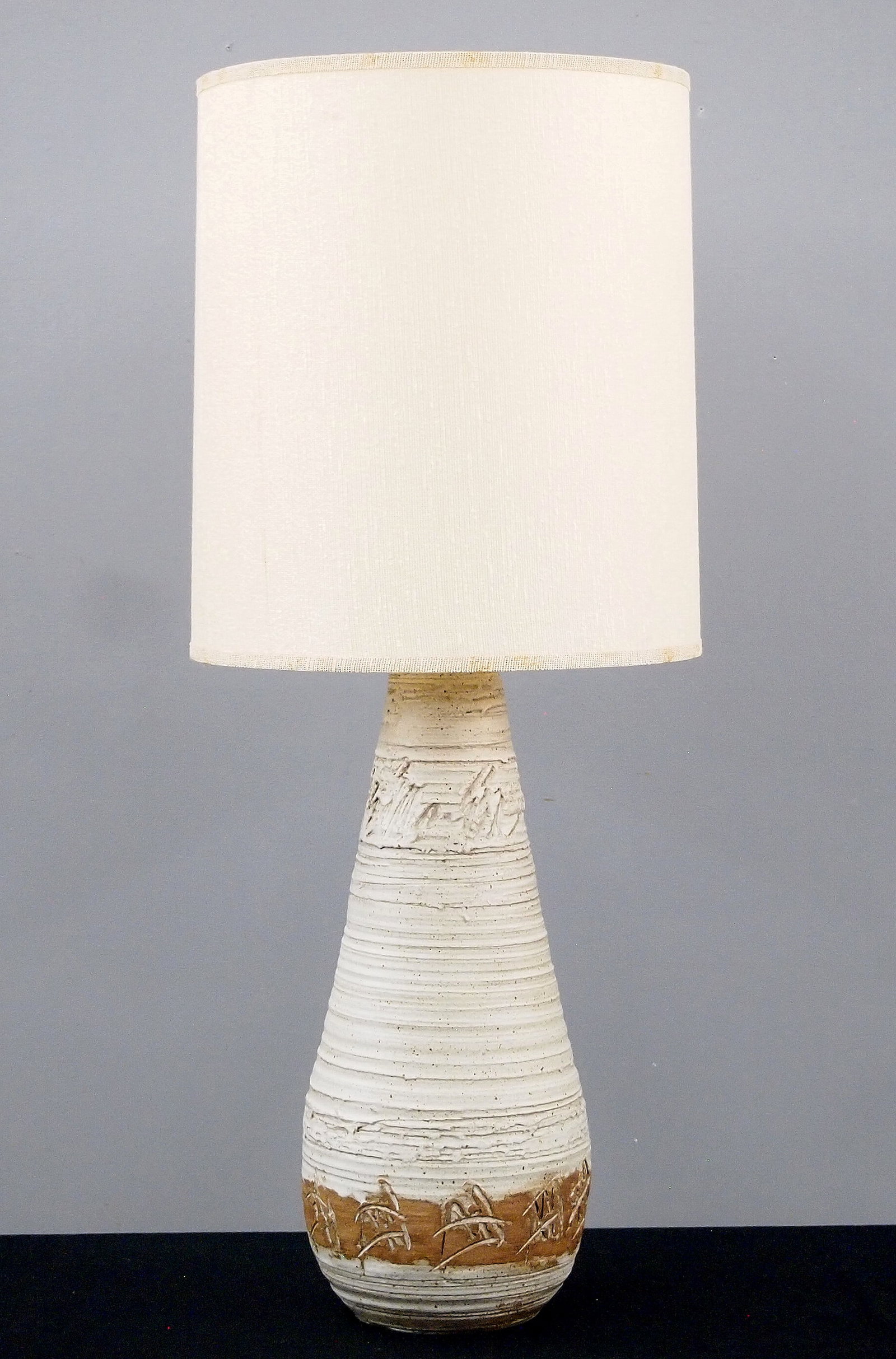 Hazen Mid Mod Stoneware Lamp: A Mid Century Modern Stoneware table lamp by Jean Hazen, Ann Arbor Potters Guild, Michigan. Tapered form with ribbed texture and mottled Beige and Tan matte glaze with a period shade. Incised "JH" mon