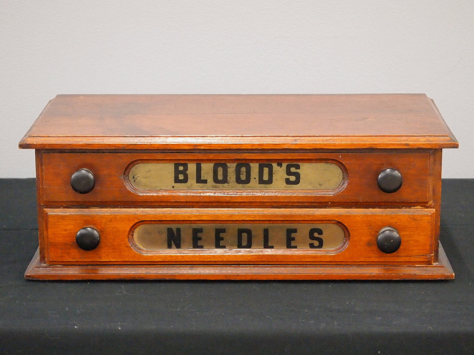 Blood's Sewing Needles Cabinet: A late 19th century Blood's counter top sewing needles cabinet. Walnut construction features two labeled dovetailed drawers with two ebonized wood knobs each. Old refinish with wear with some