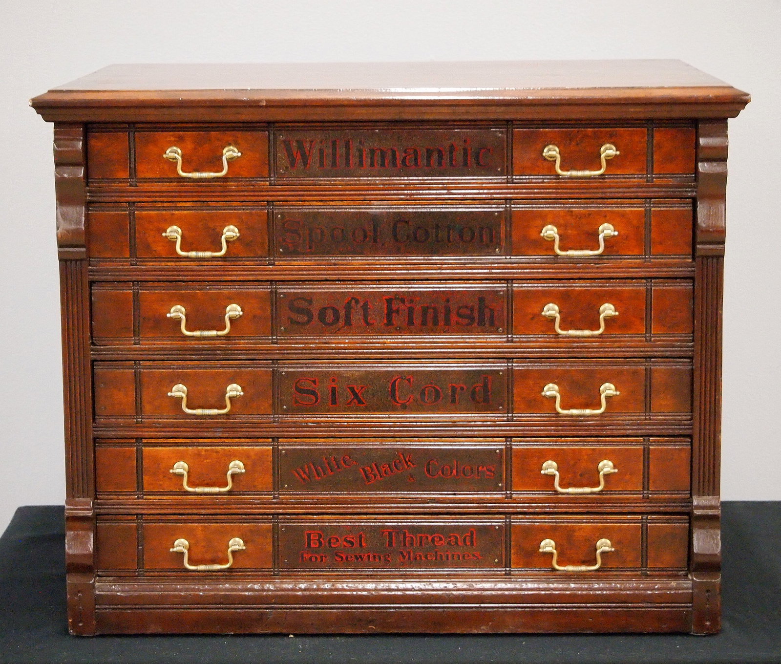 Willimantic Spool Cabinet: A 19th Century Willimantic Spool Cabinet. Walnut construction features six labeled drawers with brass handles flanked by pilasters at either side with an advertising panel verso featuring and Owl