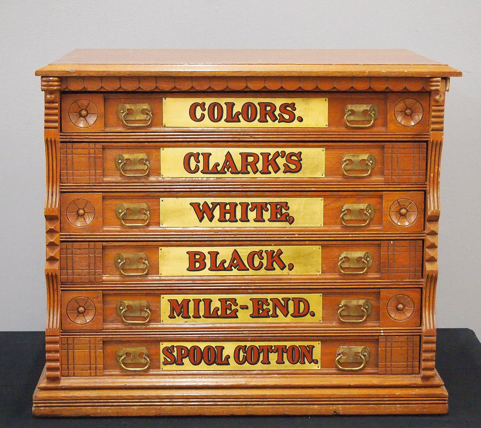 Clark's Spool Cabinet: A turn of the century Clark's Spool Cabinet. Oak construction features six labeled dovetailed drawers with brass handles and painted red and gold labels. Older refinish with some wear, replaced drawer