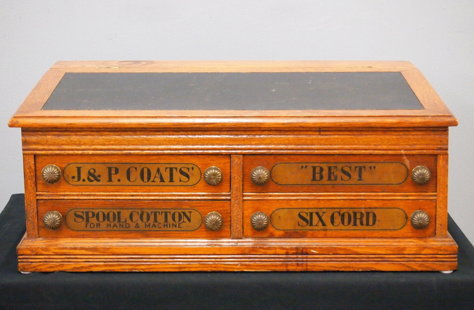 J. & P. Coats Spool Cabinet: A turn of the century J. & P. Coats Counter Top Spool Cabinet. Oak construction features a lift up writing slope over four labeled dovetailed drawers with brass knobs along with a medallion featuring 