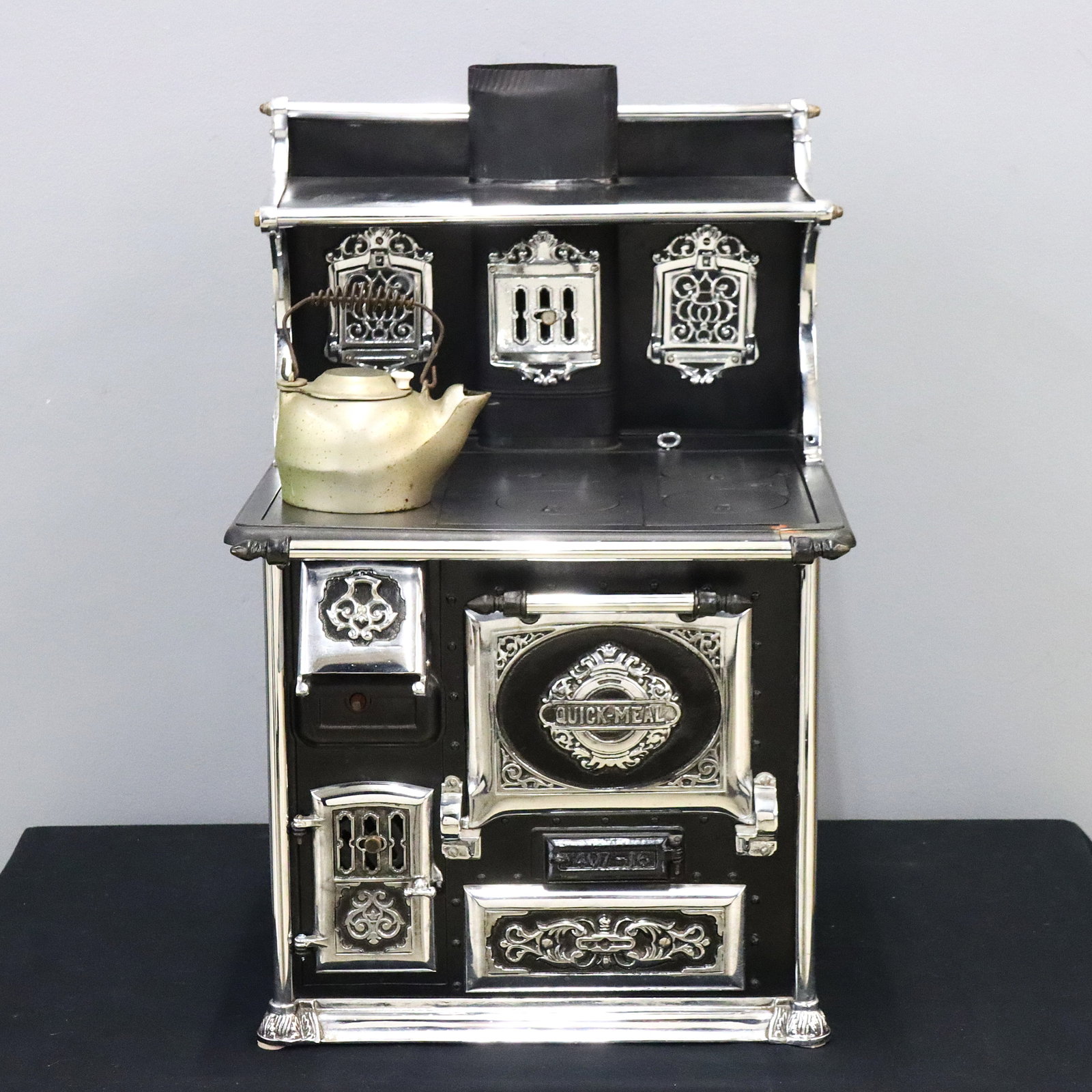 Child's Quick Meal Kitchen Stove: A turn of the century Child's "Quick Meal" wood burning kitchen stove. Cast Iron and steel construction features an upper warming shelf with fold down shelves and incorporated stovepipe, over a flat