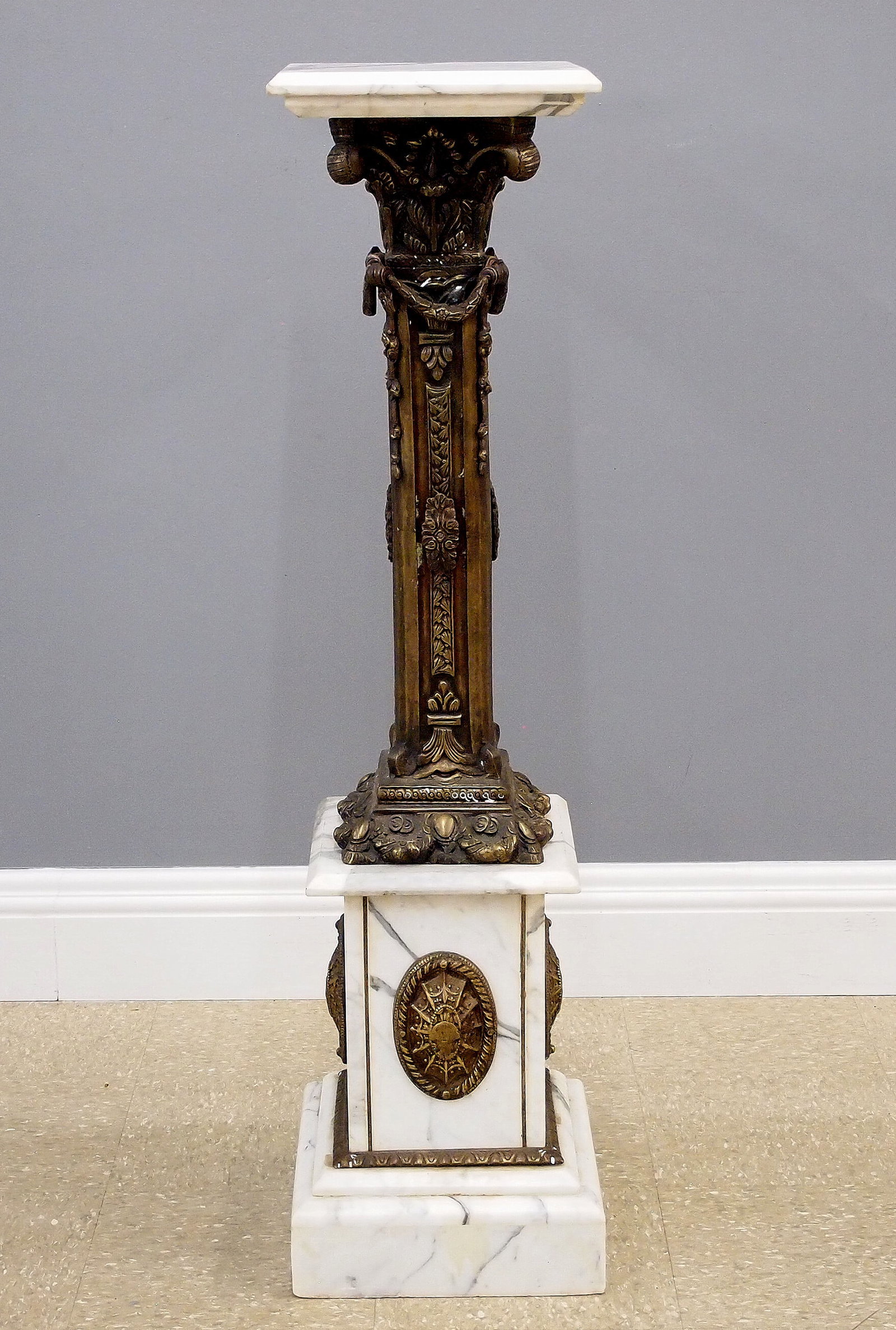 Bronze & Marble Pedestal: A late 20th century Neoclassical display pedestal. Bronze and marble construction with a cast foliate column. Some wear, repaired crack in top of base. 12 x 12 x 47 3/4" high overall. ESTIMATE