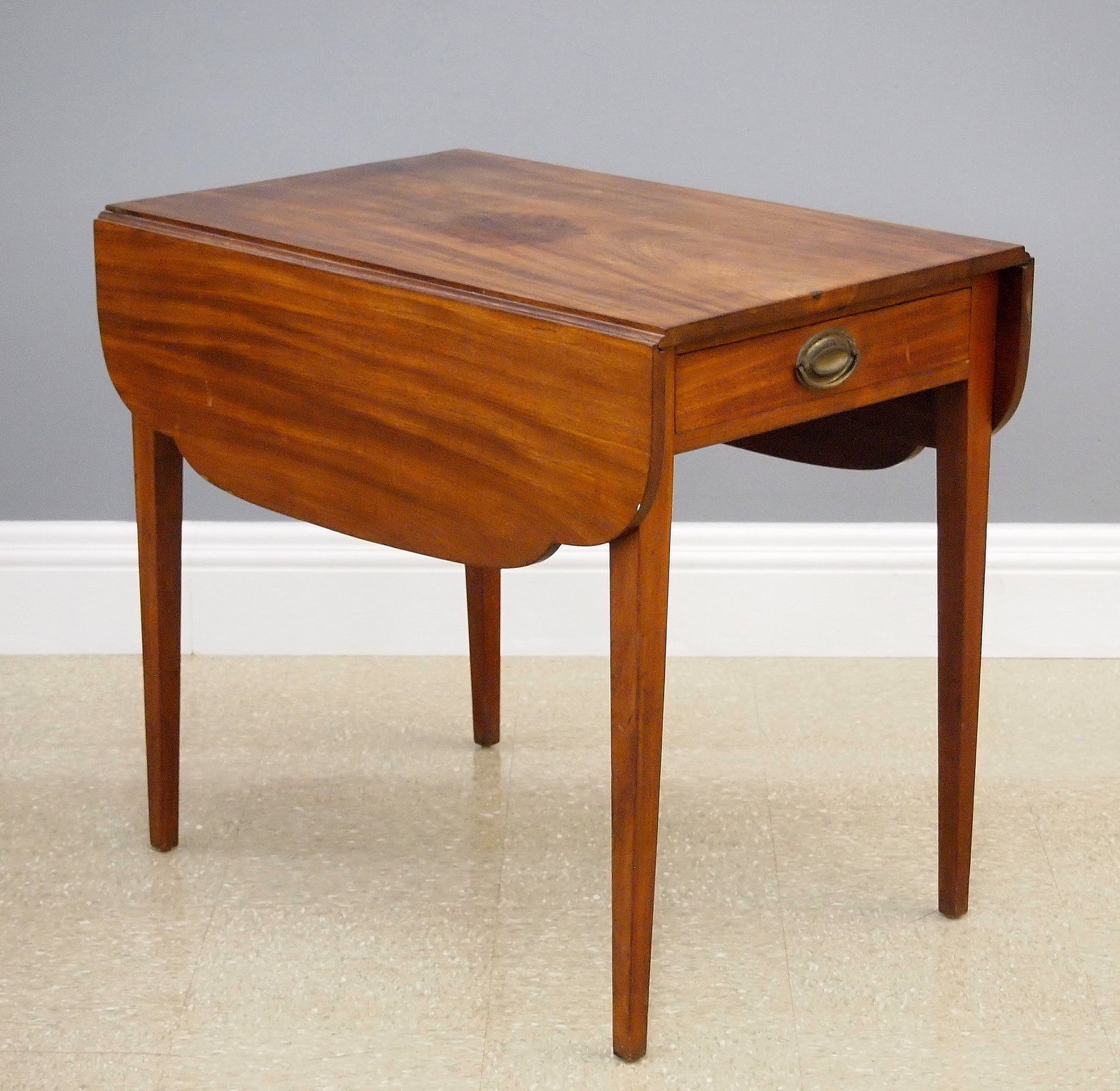 American Federal Pembroke Table: A late 18th/early 19th century American Federal Period Pembroke table. Mahogany construction features a single dovetailed drawer with original brass handle, shaped drop leaves, tapered legs. Interior 