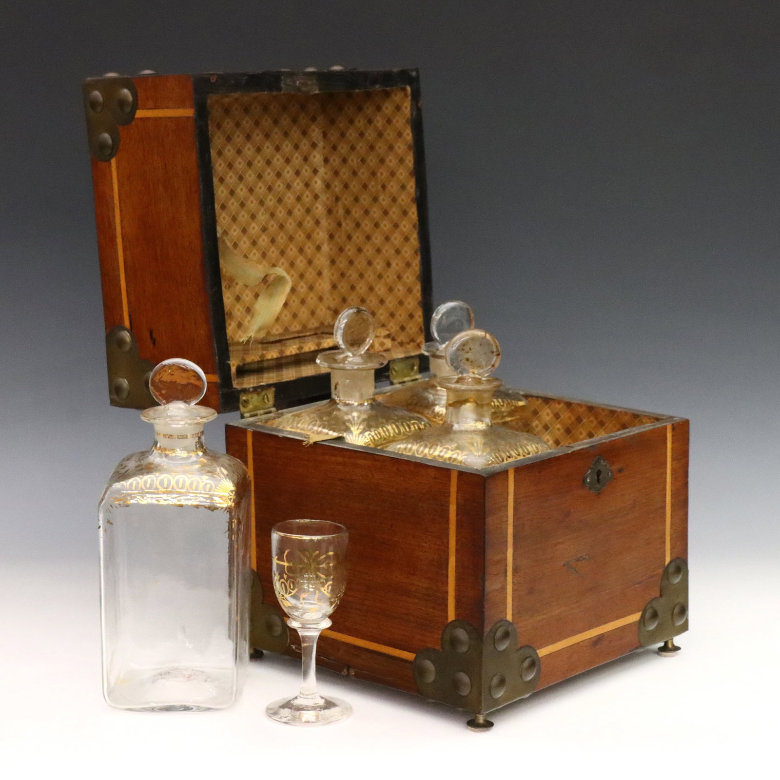 English Tantalus Set: A mid 19th century English tantalus set. Inlaid Walnut construction with Satinwood banding, studded corner mounts and flared Brass feet, hinged top opens to reveal a fitted interior with four blown gl
