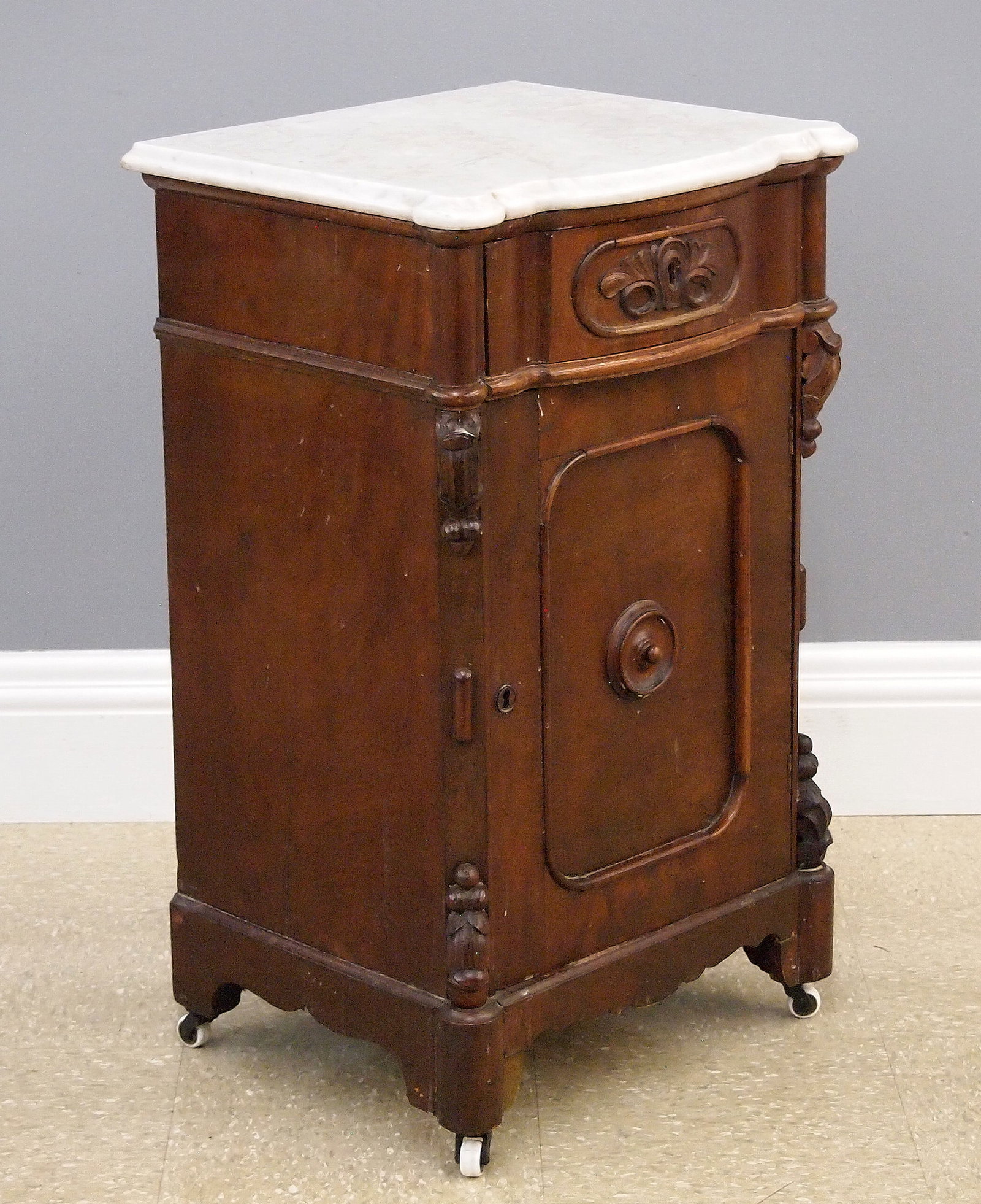 Victorian Nightstand: A late 19th century American Victorian Period Renaissance Revival night stand. Walnut construction with a shaped White marble top over a dovetailed drawer and single lower door, with applied carving a