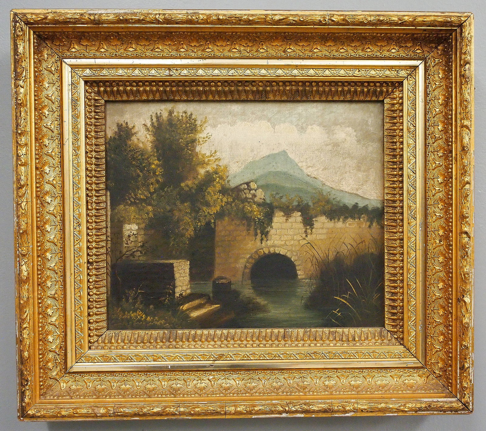 European Landscape: A late 19th century European oil on canvas landscape. Depicts a stone bridge over water surrounded by trees and tall grasses with mountains in the distance. Unsigned. Some craquelure, needs cleaning. 