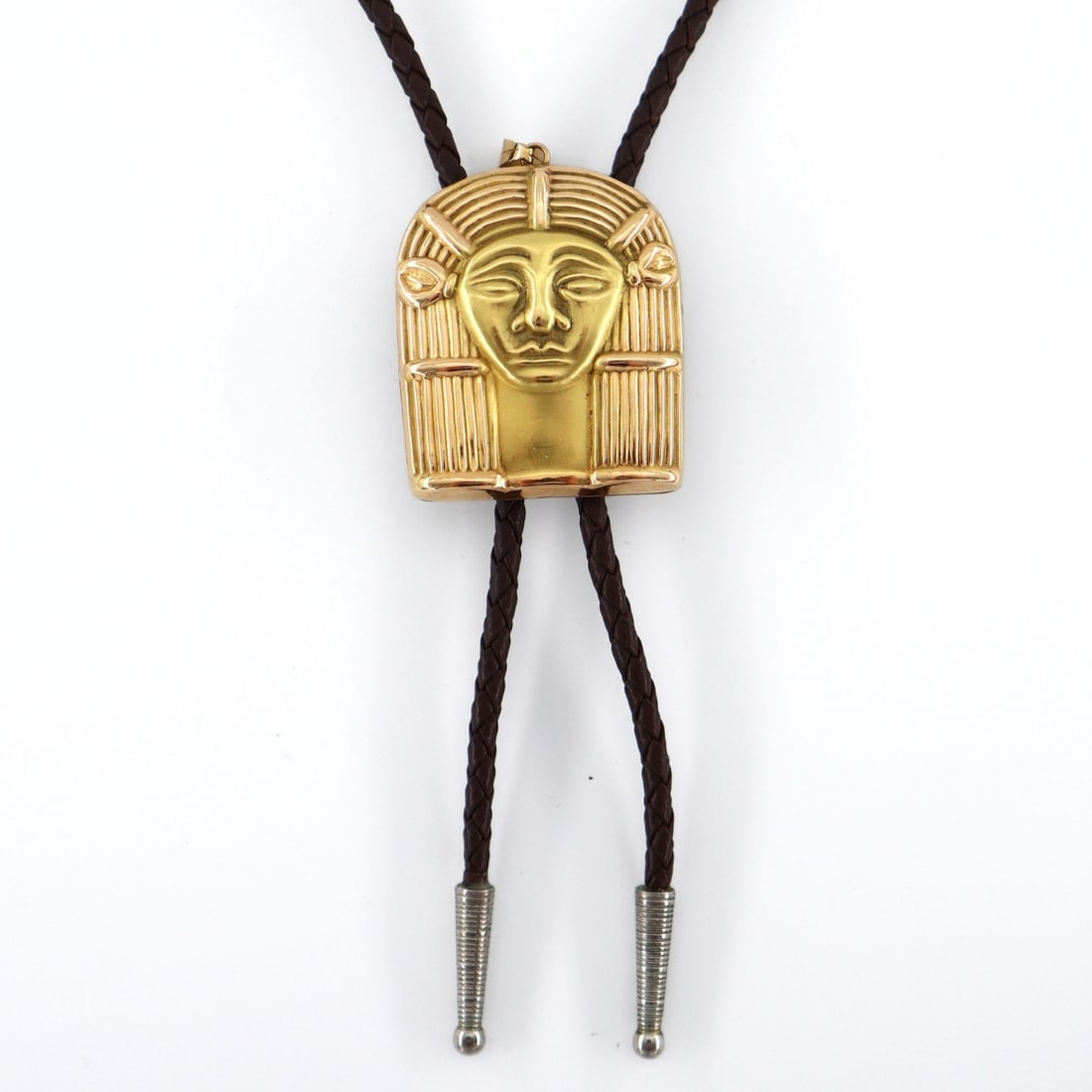 Egyptian 18k Gold Bolo Tie: A vintage Egyptian 18k Gold bolo tie. Features an 18k figural pendant depicting a mask of the Egyptian Goddess Hathor with brushed accents on a braided leather tie with Silverplated aiguillettes. Hang
