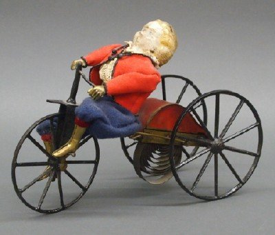 Clockwork toy: A 19th century Stevens & Brown clockwork toy Velocipede. Painted tin and cast iron tricycle with composition head rider with gilded tin arms and legs and fabric clothing. Stenciled mark "Pat'd Feb 1st