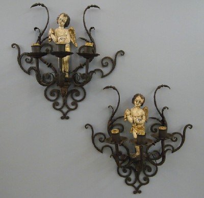Pair of Spanish sconces: A Pair of turn of the century Spanish Wrought Iron Sconces. Each with a polychrome wood and gesso figure of a putto and three lights. Wear to each, with minor losses to the figures. 26 x 27" high. EST