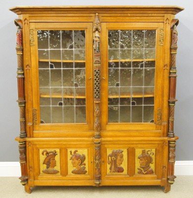 Gothic Revival china cabinet: A 20th century Gothic Revival Period Oak china cabinet. Molded crown over two doors with stained glass panels, flanked on either side by carved posts with paint decorated figural finials, on a two doo