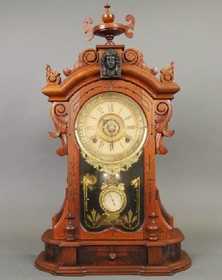Ansonia "Monarch" Clock: A Turn of the Century Ansonia "Monarch" Mantle Clock. Eight day time and strike movement with Paper dial. Consisting of a Walnut case with urn form finial above carved scroll and Female mask motif, br