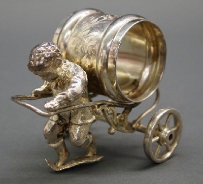 19th Century Figural Napkin Ring: A 19th Century American Silver Plate Figural Napkin Ring. Figure of a little Boy, with ruffled collar, pulling a cart with a Napkin ring atop of it. No apparent markings. Some wear to the silver. 3" h