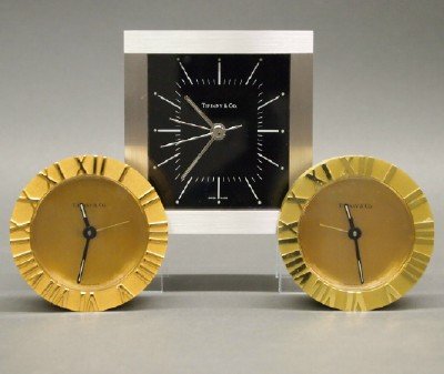 3 Tiffany & Co. Clocks: A Group of Three Tiffany & Co. Clocks. Including Two brass "Atlas" table clocks and One rectangular white metal desk clock. All are battery operated and Swiss made. Minor wear to each. Up to 3 1/2" hi