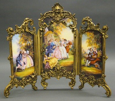 Austrian Enameled Screen: A Turn of the Century Austrian Table Screen. Three enameled decorated panels, together as one continuous scene, depict an exterior scene with couples playing Blind Man's Bluff; set within an ostentati