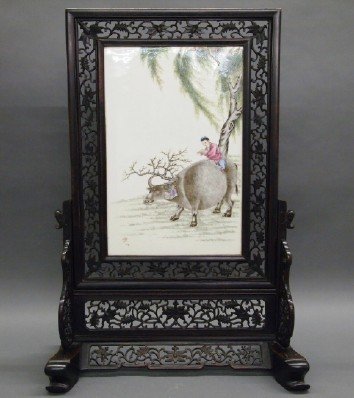 Chinese Porcelain Table Screen: A Chinese Enameled Porcelain Table Screen. Having an enamel decorated Porcelain plaque, with a motif of a boy riding atop a Water Buffalo, that is situated within an intricately carved wood frame and 