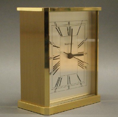 Tiffany & Co. Clock: A Tiffany & Co. Brass Mantle Clock. Having a rectangular brass case and black Roman Numerals printed on the metal the dial. Stamped "Made in Germany". Battery operated. Very minor wear. 5 3/4" high. E