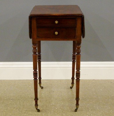 Sheraton Sewing table: A 19th century English Sheraton Period Mahogany sewing table. Molded drop-leaf top above two dovetailed drawers and two additional faux drawers on slender turned legs terminating in Brass cup castors.