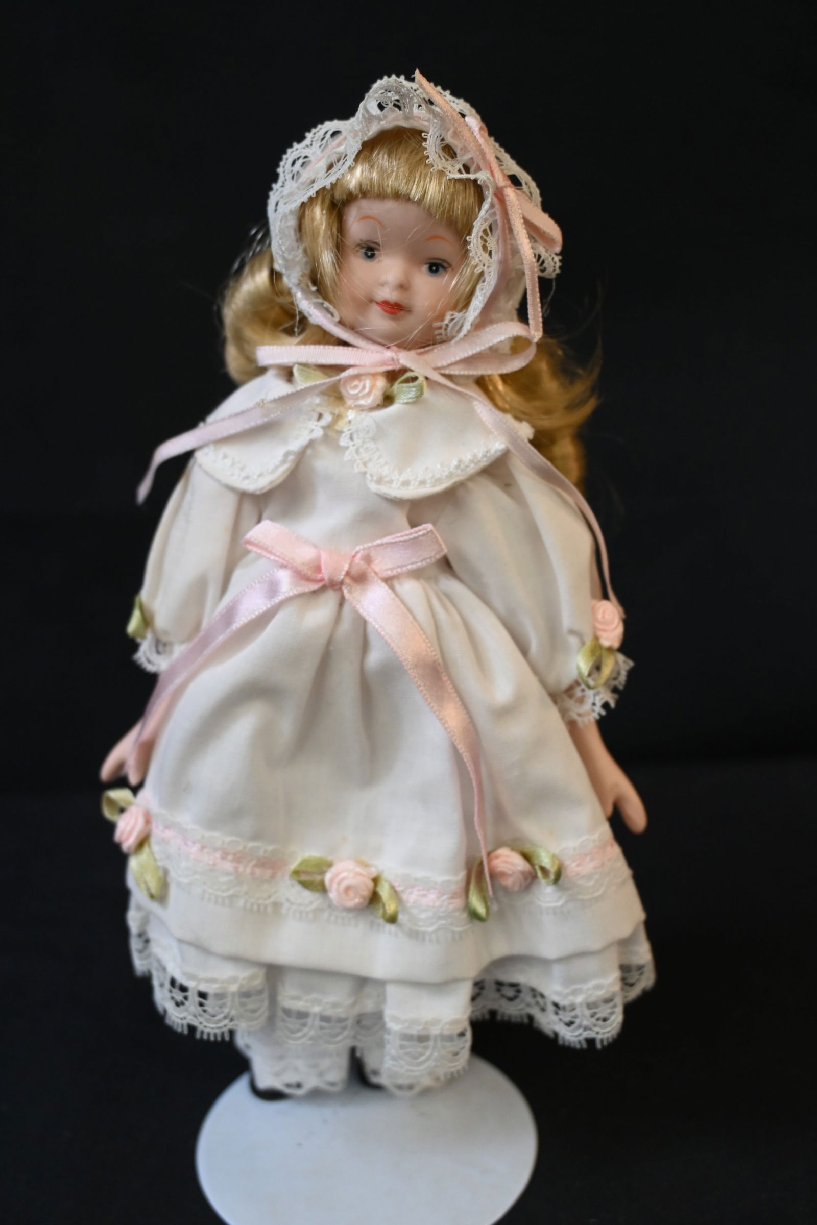 Vintage 8” Porcelain & Fabric Doll – Small Collectible: This vintage 8-inch doll features a porcelain head, hands, and feet with a soft, stuffed fabric body. She is dressed in a charming cotton dress with ruffles, lace, and ribbon rose trim, complemented b